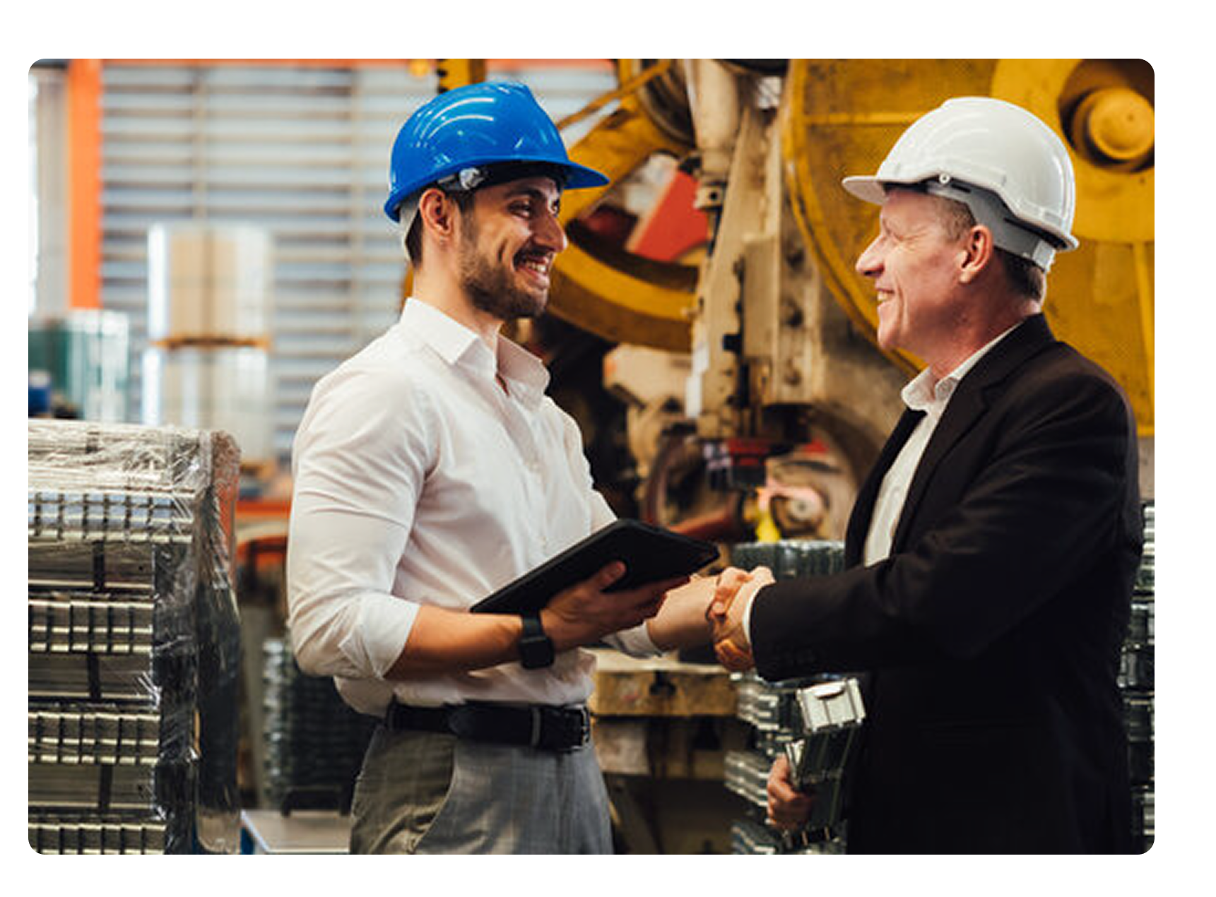 Two men in a manufacturing plant smiling and shaking hands